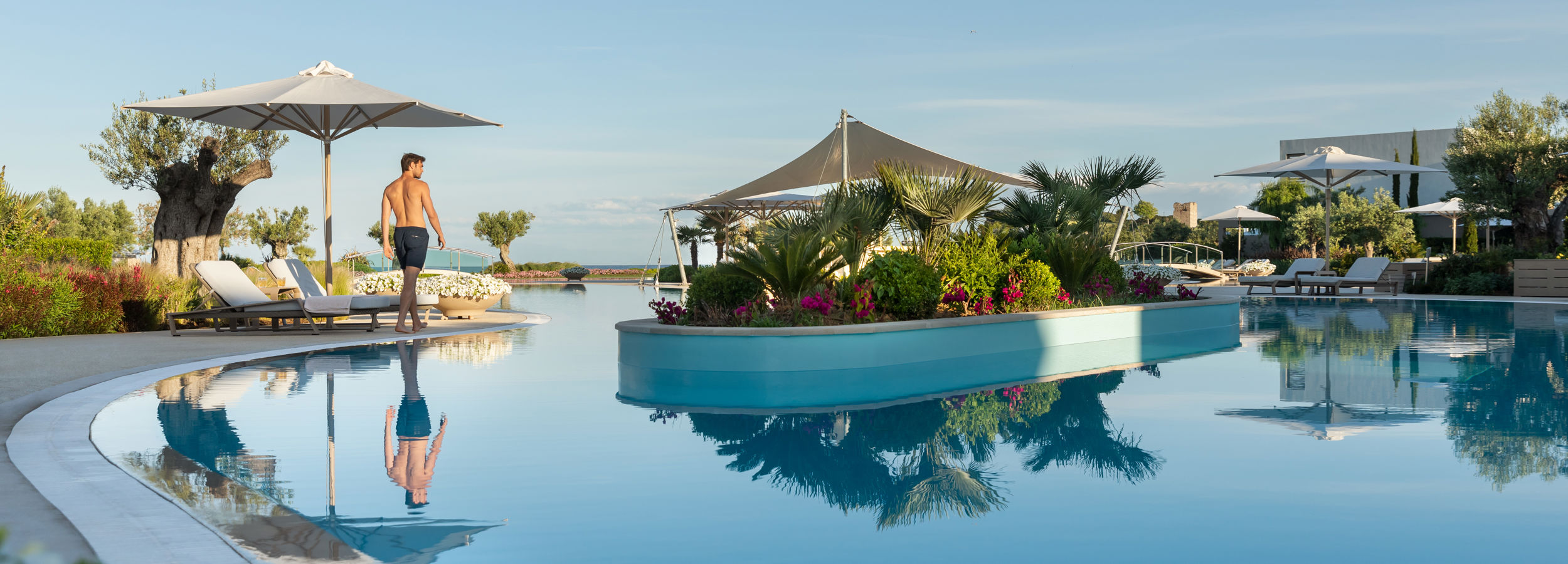 Uomo che cammina intorno alla piscina riscaldata del Sani Dunes con vista sul resort
