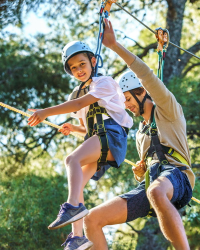 Father and daughter playing together on treetop high ropes 