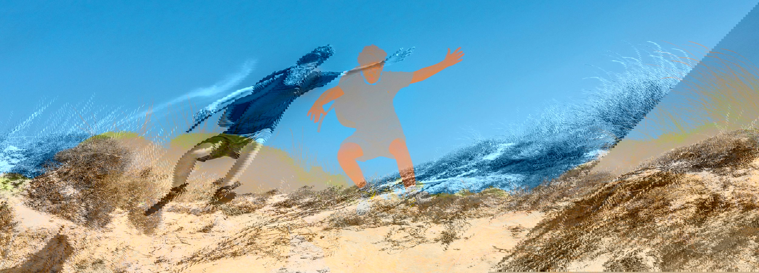 Junge springt auf Sanddünen im Bear Grylls Survival Academy Beach Survival Camp