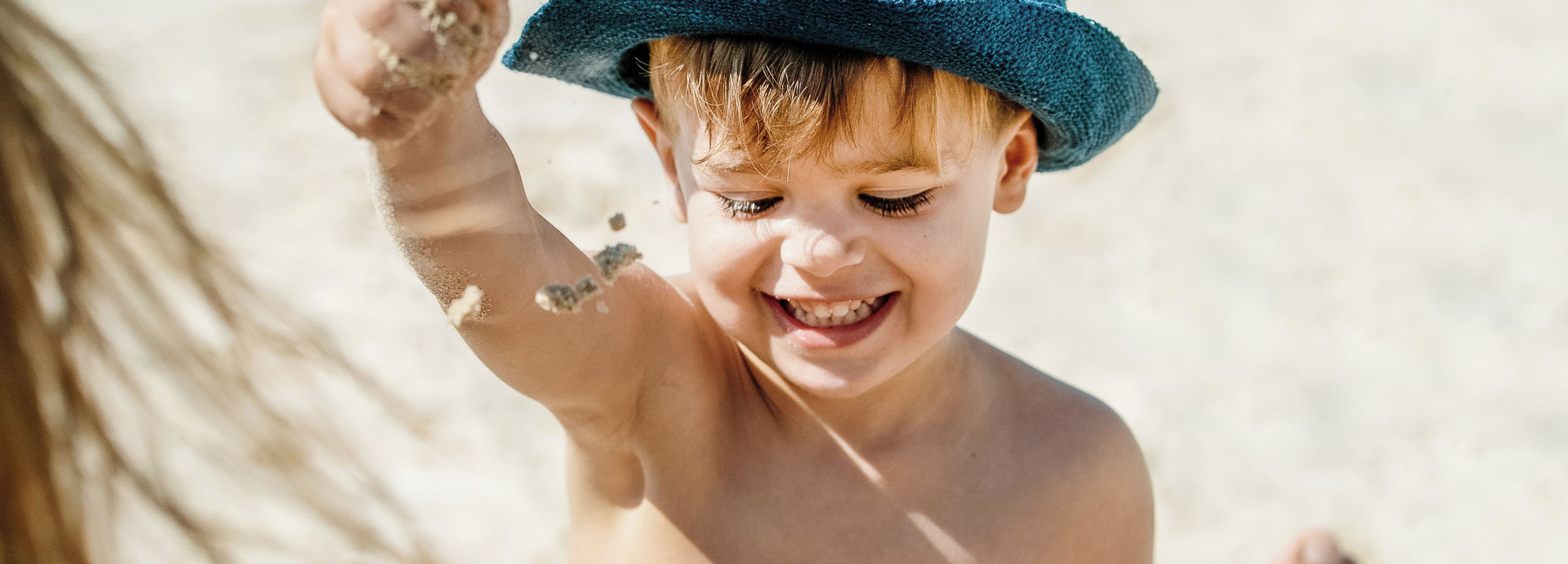 Petit garçon portant un chapeau de soleil jouant avec du sable